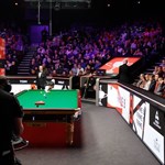 A snooker table is set up and a crowd waits for the frame to start.