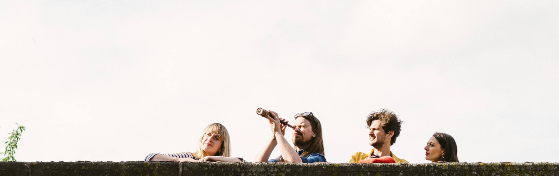 Four people looking over a high wall, one with a telescope, playing Treasure Hunt Sheffield.