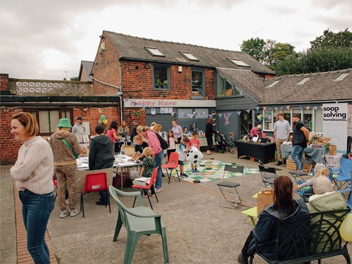 A group of people gathered together in a court yard, socialising with family craft activities taking place