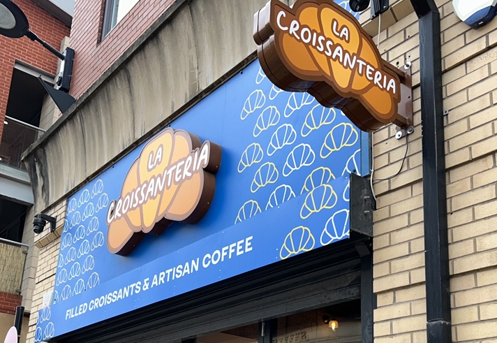 A side view of the sign outside of the shop, which reads La Croissanteria, the title is placed on top of croissant