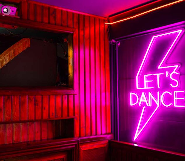 A pink neon sign with a lighting bolt and the words 'Let's Dance'.