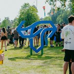 A giant sculpture of the Tramlines festival logo stands on the grass as a crowds of festivalgoers walk by