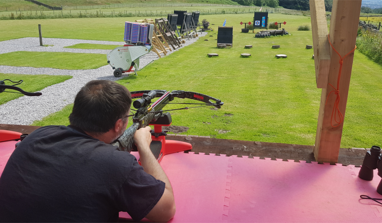 A person firing a crossbow at a target on a shooting range.