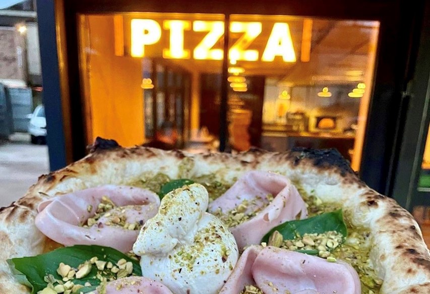 Urban Pizza Co.'s signature mortadella and pistachio pizza held up in front of their  site at Steel Yard Kelham