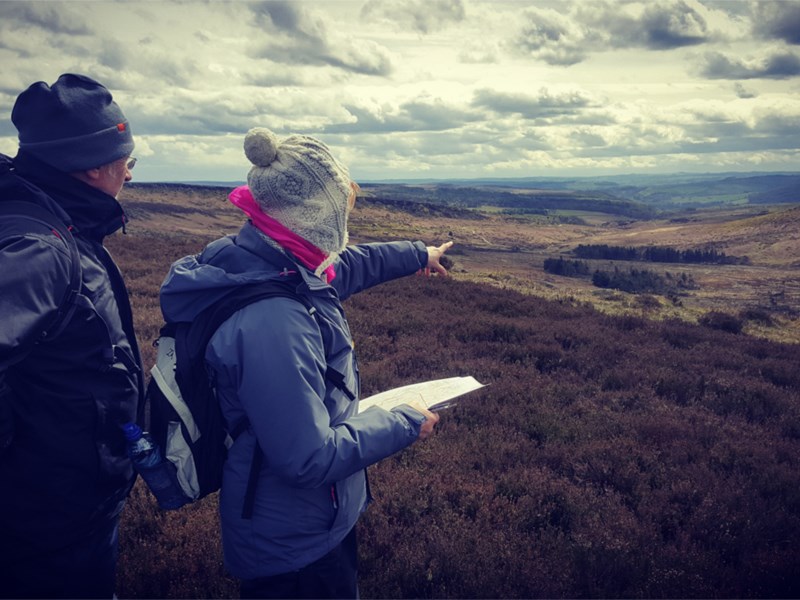 Two people out walking in the countryside, one of them is holding an open map.