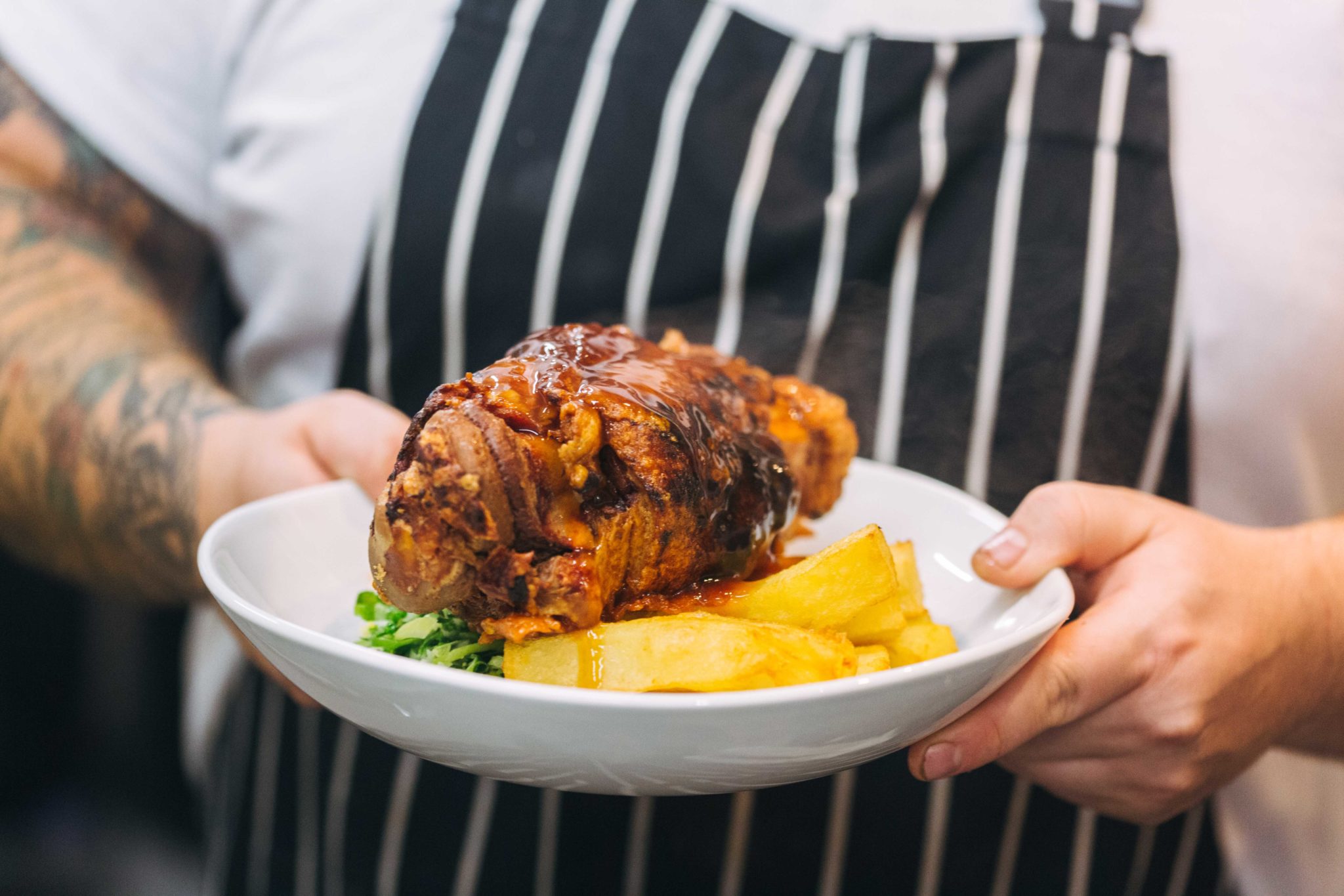 A man in a blue and white striped apron carries a plate of food.
