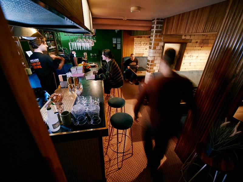 Interior shot of Public, a cocktail bar in the centre of Sheffield. There are people sat in booths and at the bar, where a barman is serving drinks.