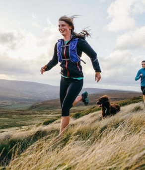 Three people are running in the countryside with their dog.