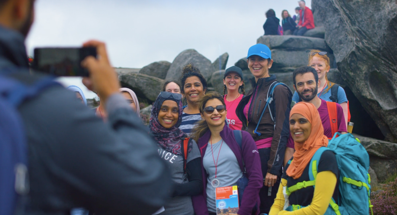 A group of people, out walking, stop next to a rocky outcrop to have a photo taken.