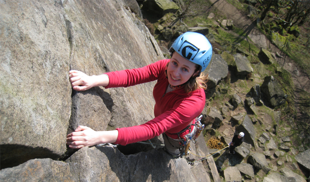 A woman climbing a rock face. She is smiling.