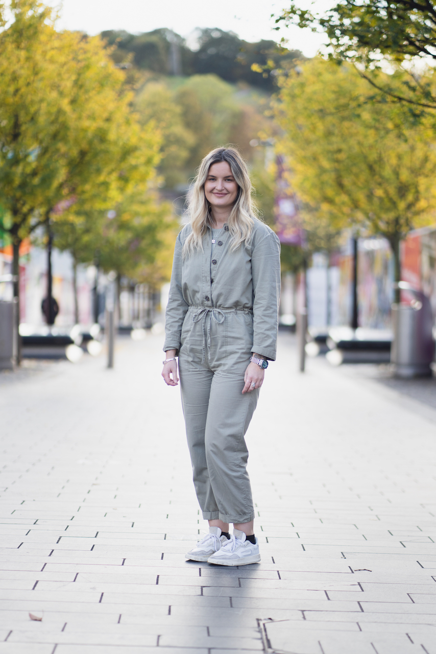 A woman poses in a grey jumpsuit.