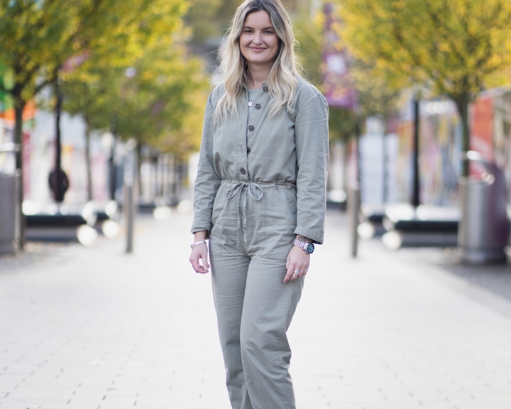 A woman poses in a grey jumpsuit.