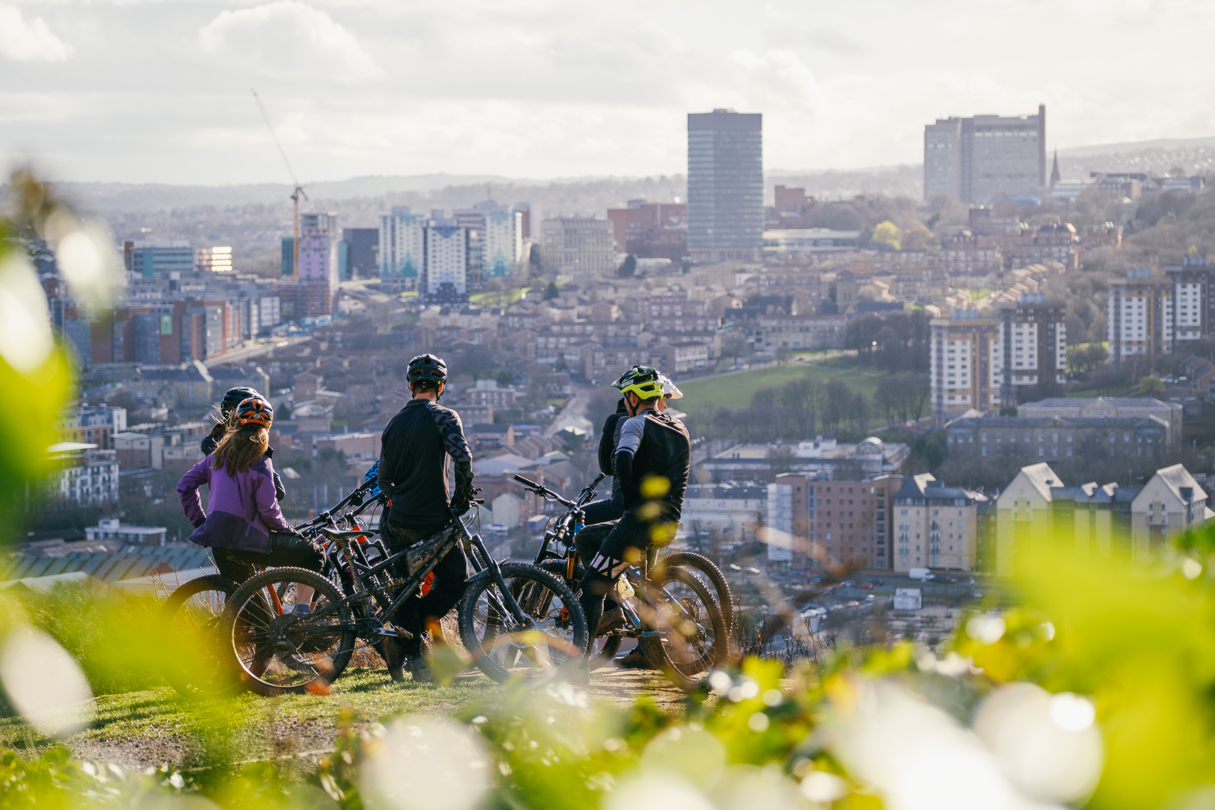Five people on mountain bikes rest for a moment at the top of Parkwood in Sheffield. In the background you can see the city centre.