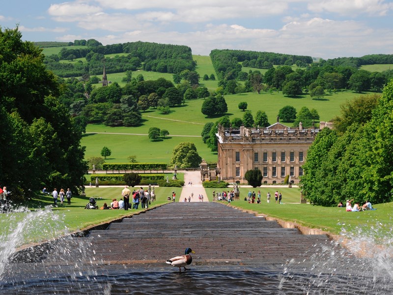 A water feature running down a hill with Chatsworth House in the distance.