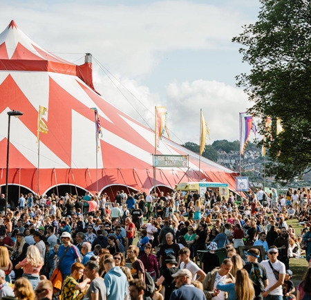 A crowd of people at the 2019 Tramlines Festival at Hillsborough Park in Sheffield. In the centre of the picture is a huge red and white circus-style tent.