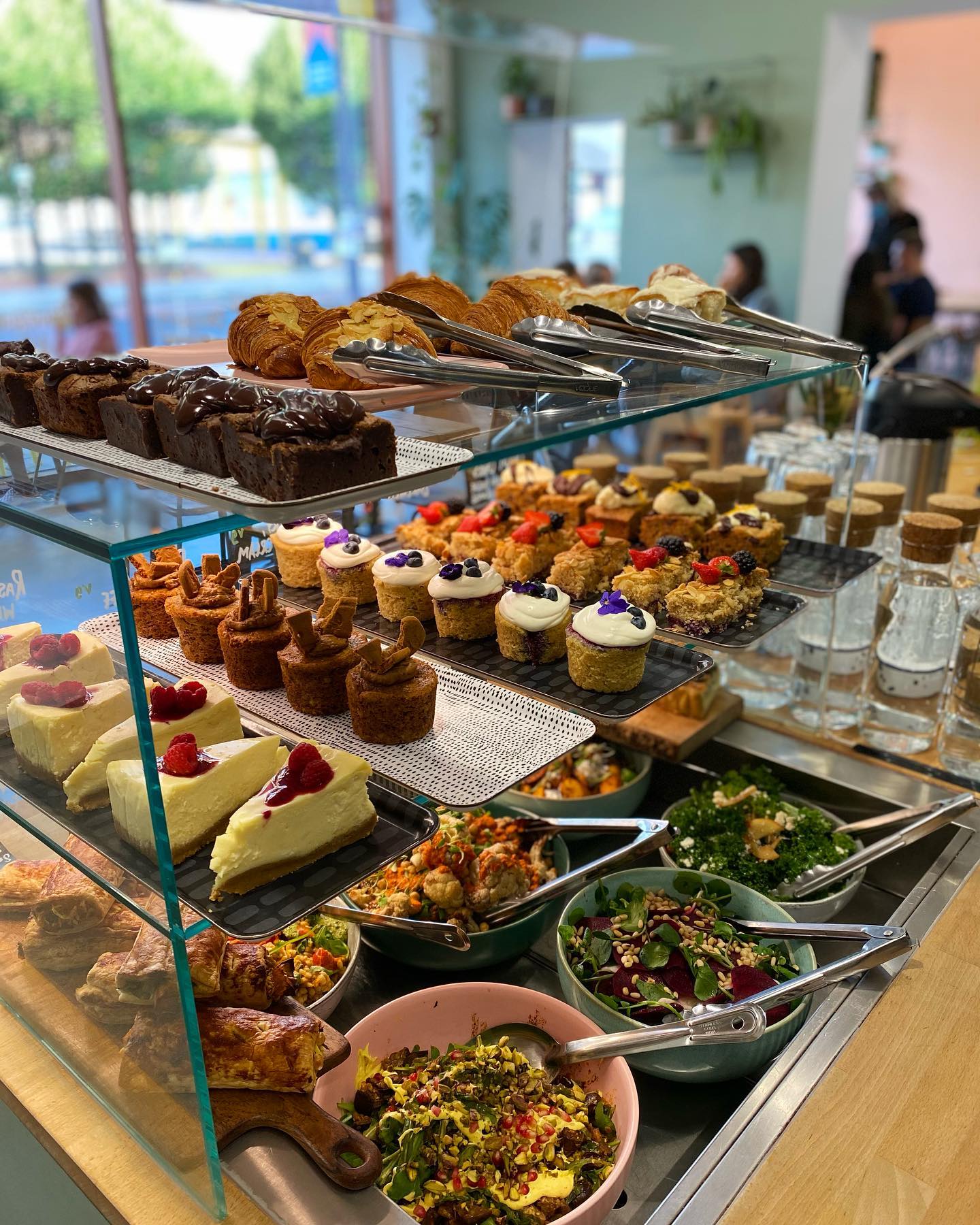 A glass display case on a counter filled with cakes, pastries and salads at Kollective Café.