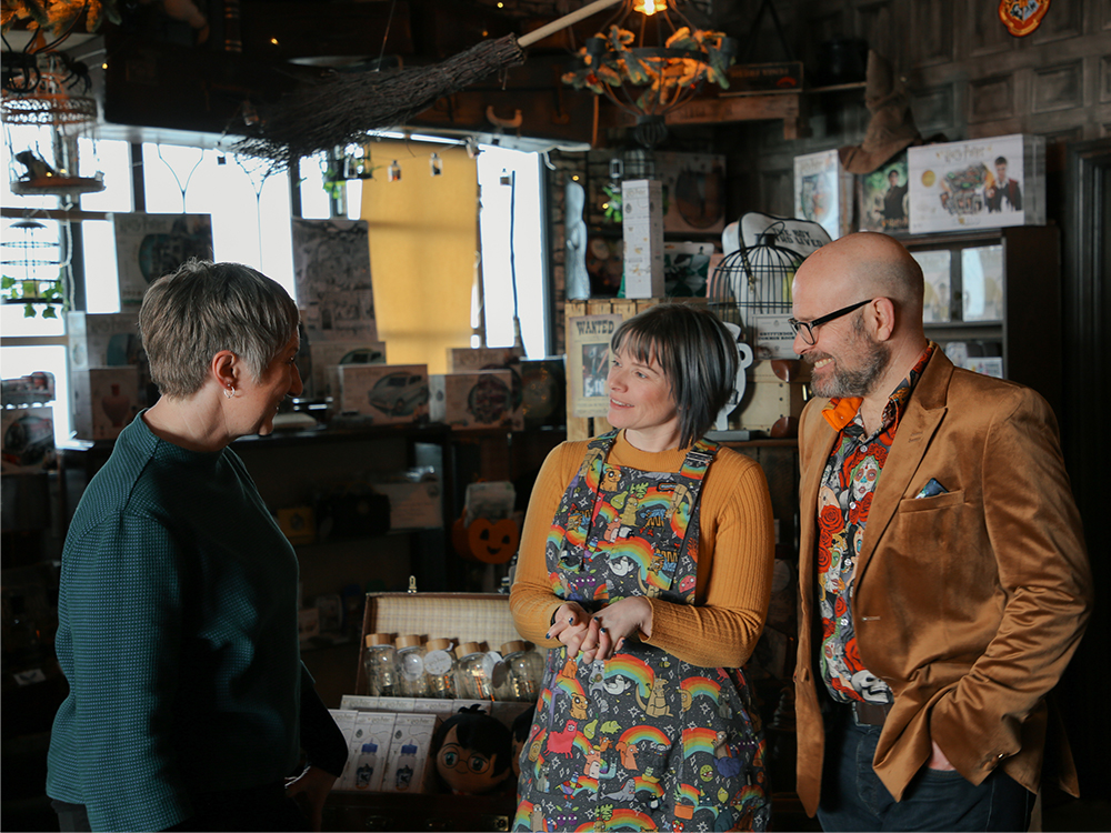 The owners and a business advisor stand in a bohemian café and shop with a wizarding theme.
