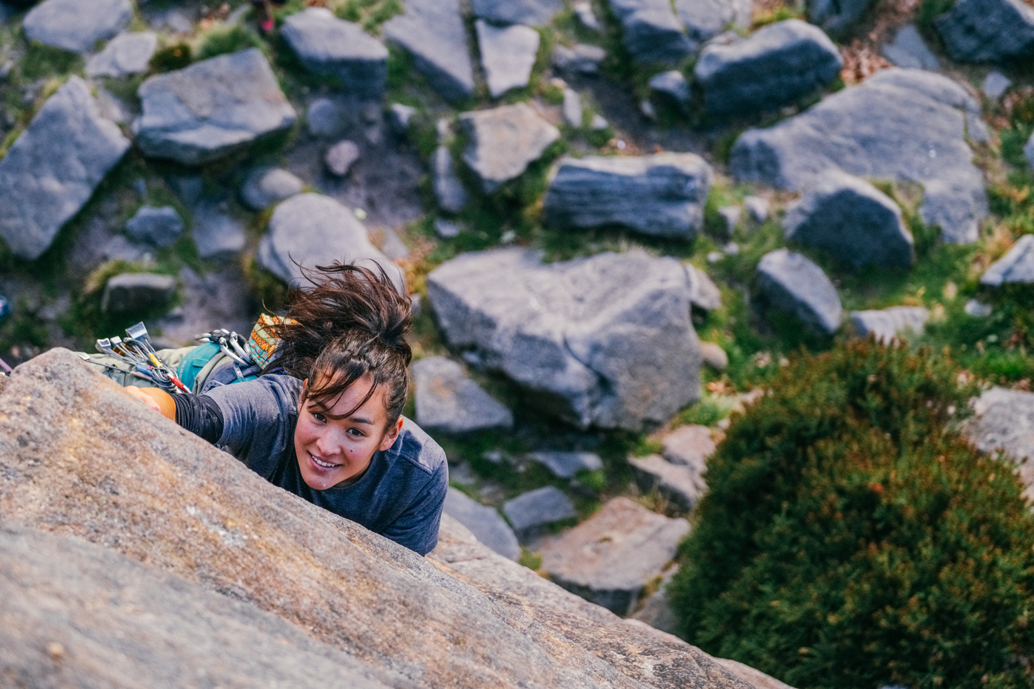 A woman climbing up a rock face as seen from above. She is clearly having fun and is determined to reach the top.