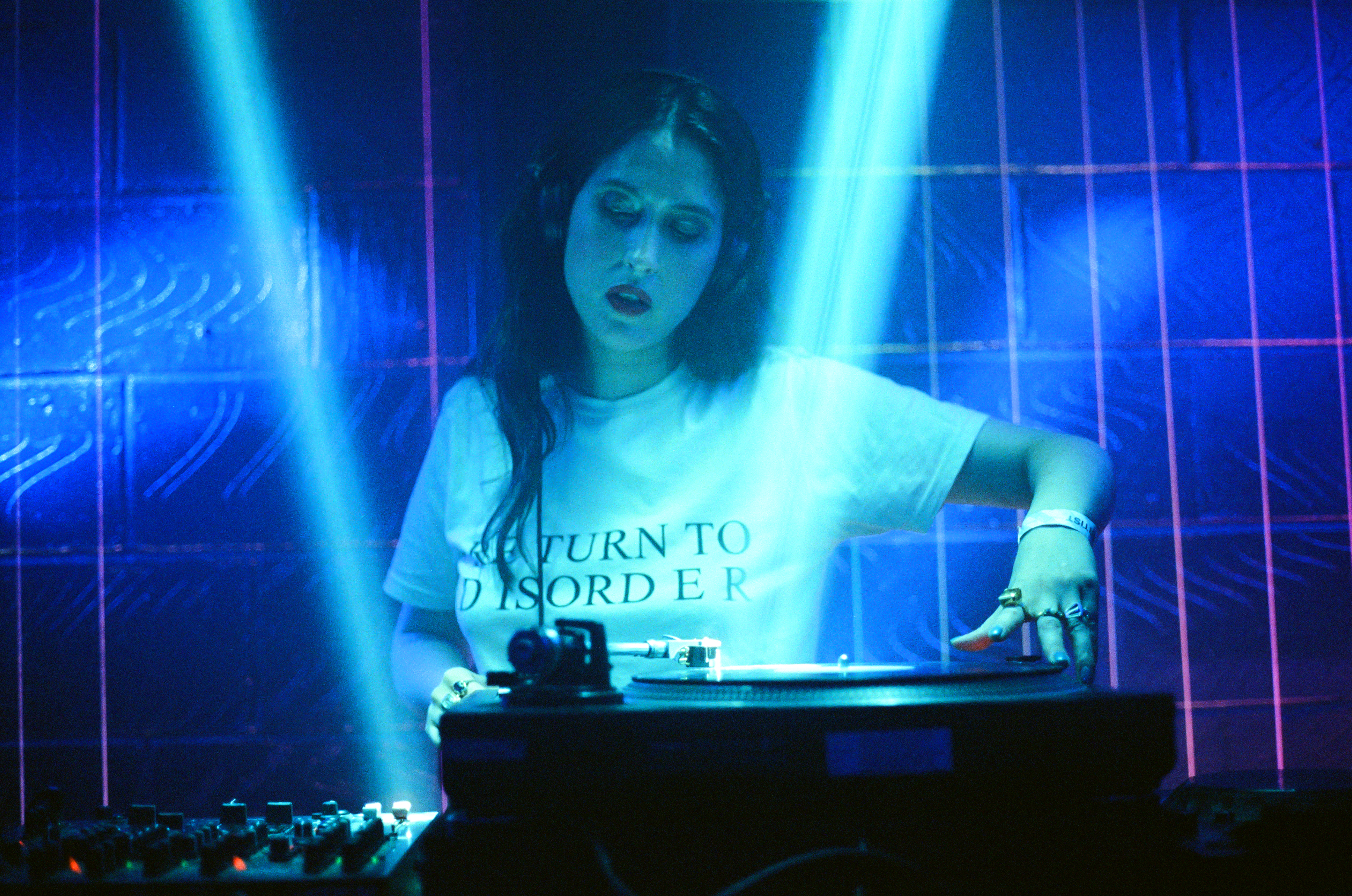 A woman mixing at a DJ deck. The room is bathed in blue light.