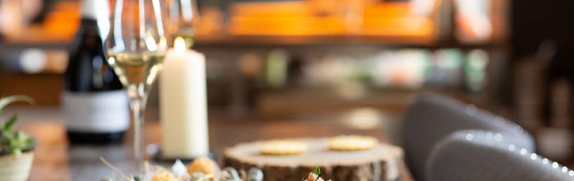 A table at a restaurant with small plates and bowls of food , a glass of wine and a candle.