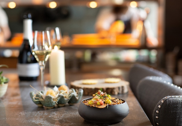 A table at a restaurant with small plates and bowls of food , a glass of wine and a candle.