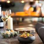 A table at a restaurant with small plates and bowls of food , a glass of wine and a candle.