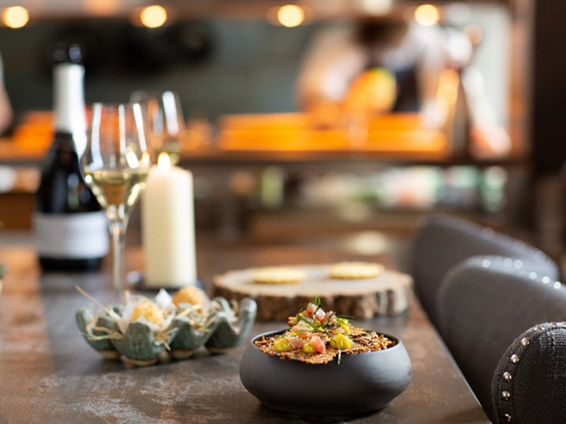 A table at a restaurant with small plates and bowls of food , a glass of wine and a candle.