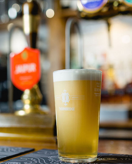 A pint a beer that has just been poured on a pub bar top.