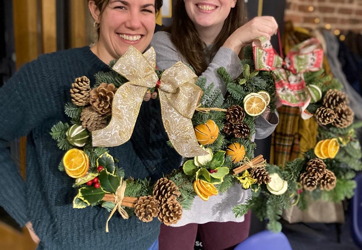 Two women proudly holding Christmas wreaths that they have made.