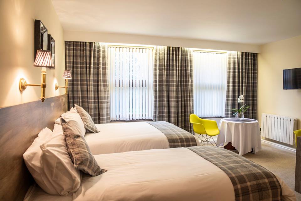 Hotel room with two double beds, beige furnishings, and a small table in the corner.