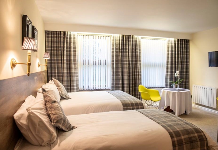 Hotel room with two double beds, beige furnishings, and a small table in the corner.