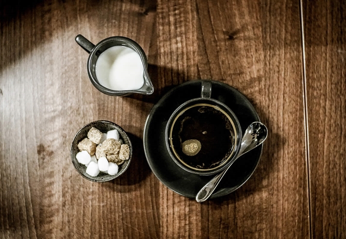 Overhead shot of a cup of coffee with a bowl of sugar cubes and a small metal jug of milk at Inox Dine.