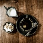 Overhead shot of a cup of coffee with a bowl of sugar cubes and a small metal jug of milk at Inox Dine.