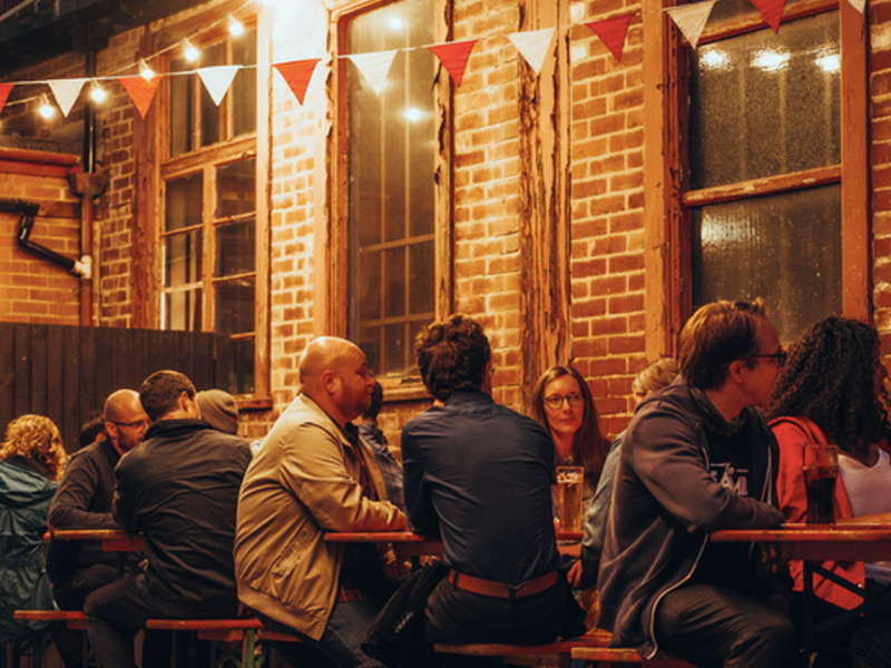 A group of people sat at tables outside, at night, having a night out.