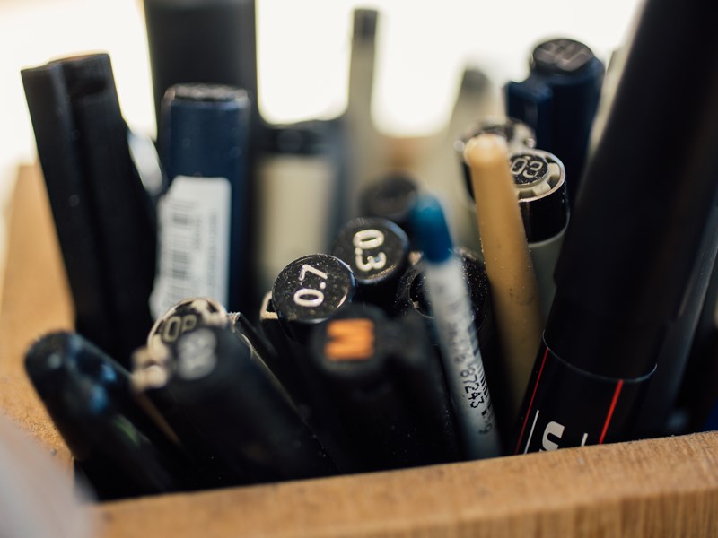 A close up of a wooden pot full of pens and pencils.