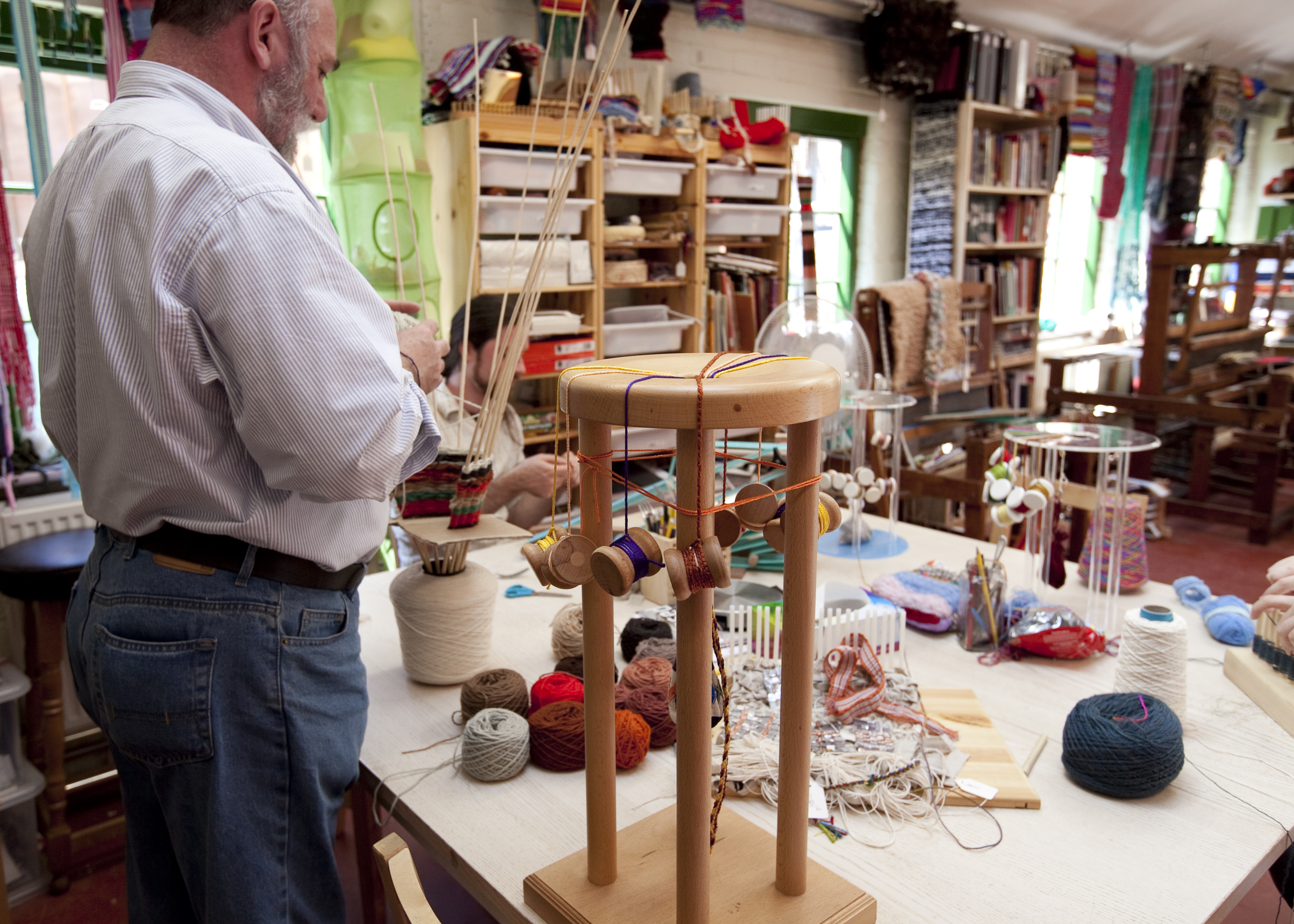 A man works in a studio, creating artworks out of different coloured wools.