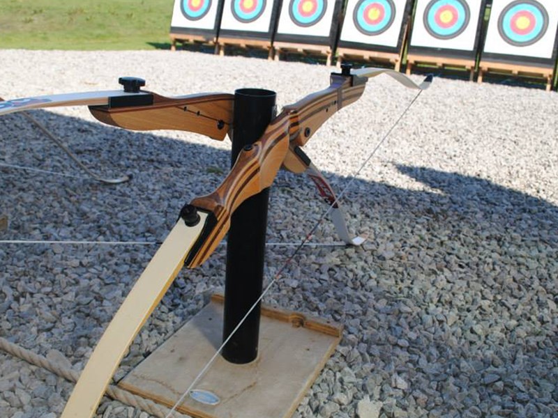 Two bows on a stand, in the distance is a row of archery targets.