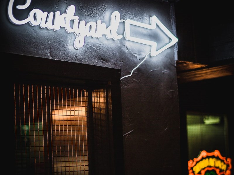 A white neon sign that reads 'Courtyard' on the wall at Monk Bar.