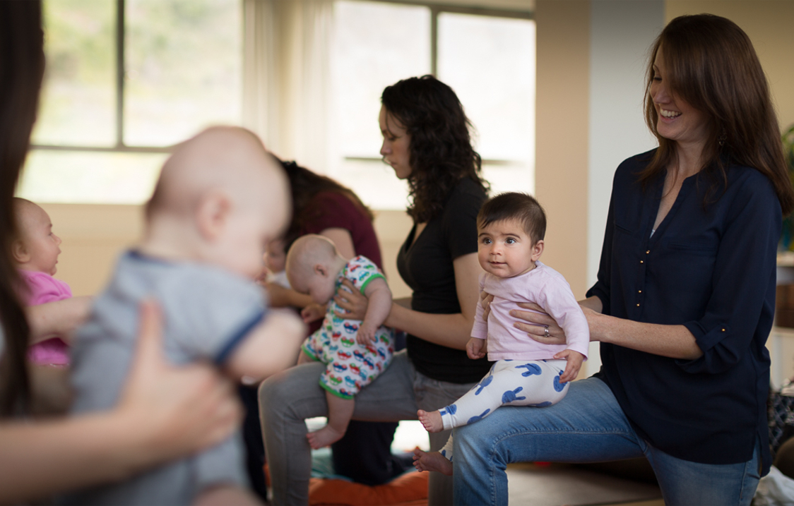 A group of mothers, holding their babies, in a yoga class.