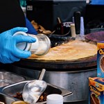 A stall trader is shaking sugar on a fresh crepe.