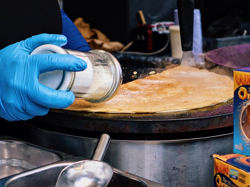 A stall trader is shaking sugar on a fresh crepe.