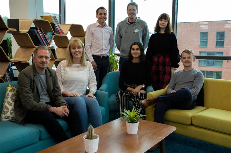 A group of seven men and women pose for a photo in an office.