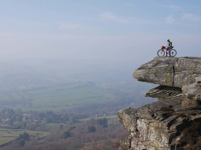 A person, on a mountain bike, on top of a rocky outcrop.