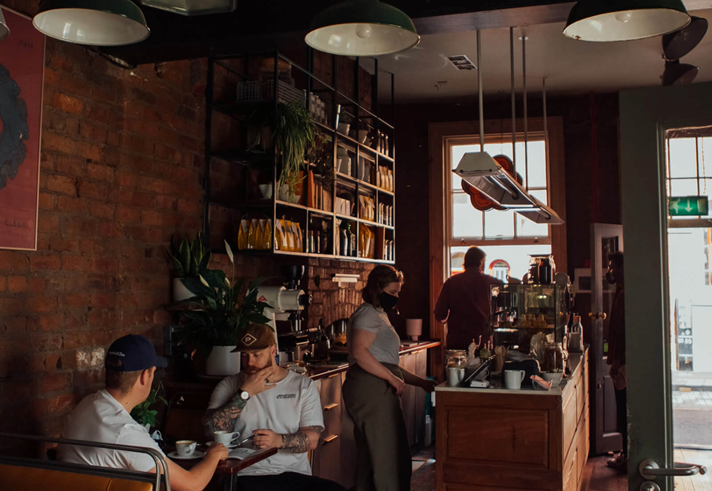 The interior of Mow's Coffee, with staff behind the counter and people drinking coffee and chatting at tables.
