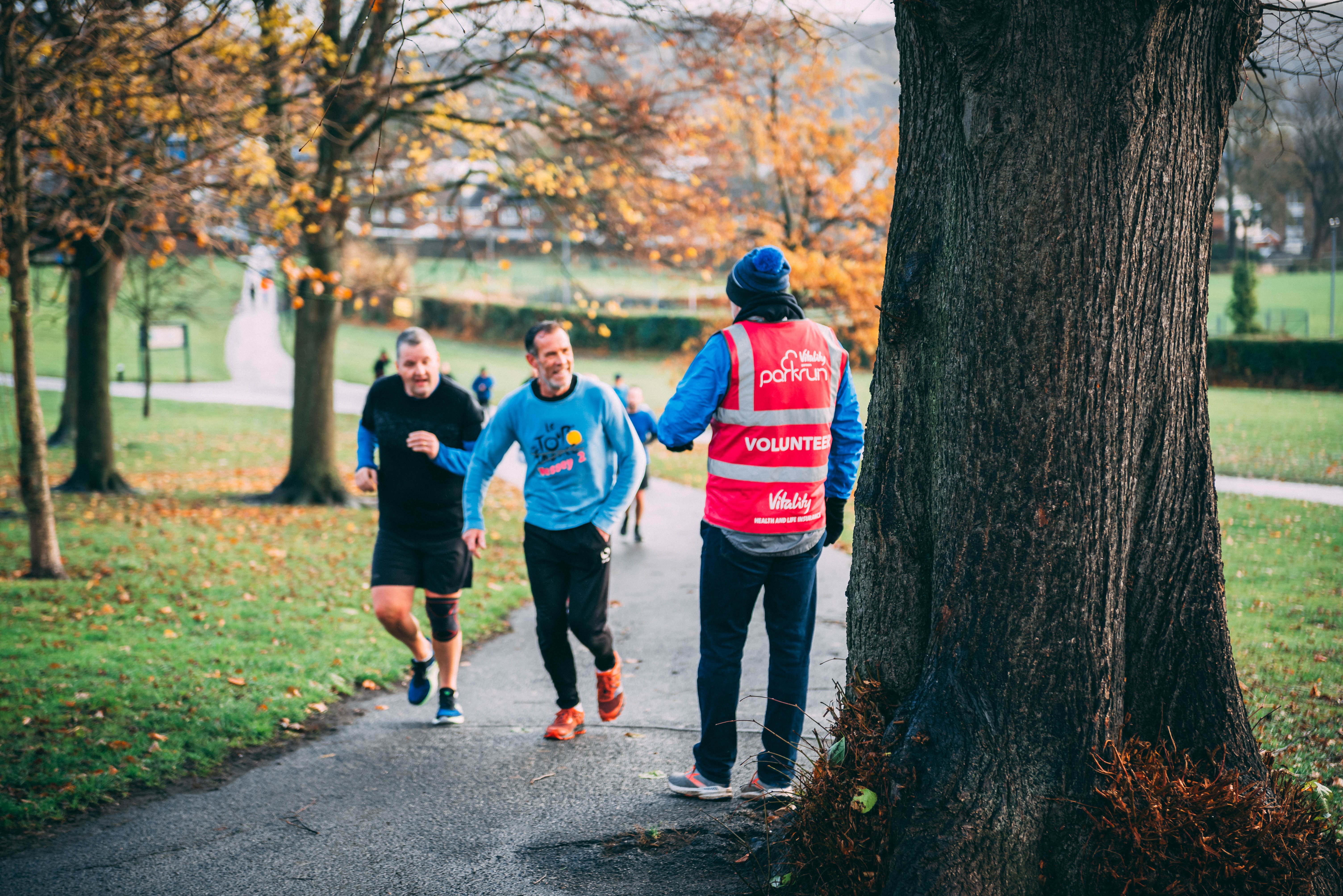Two runners participating in a Hillsborough park run, talking to a park run volunteer.