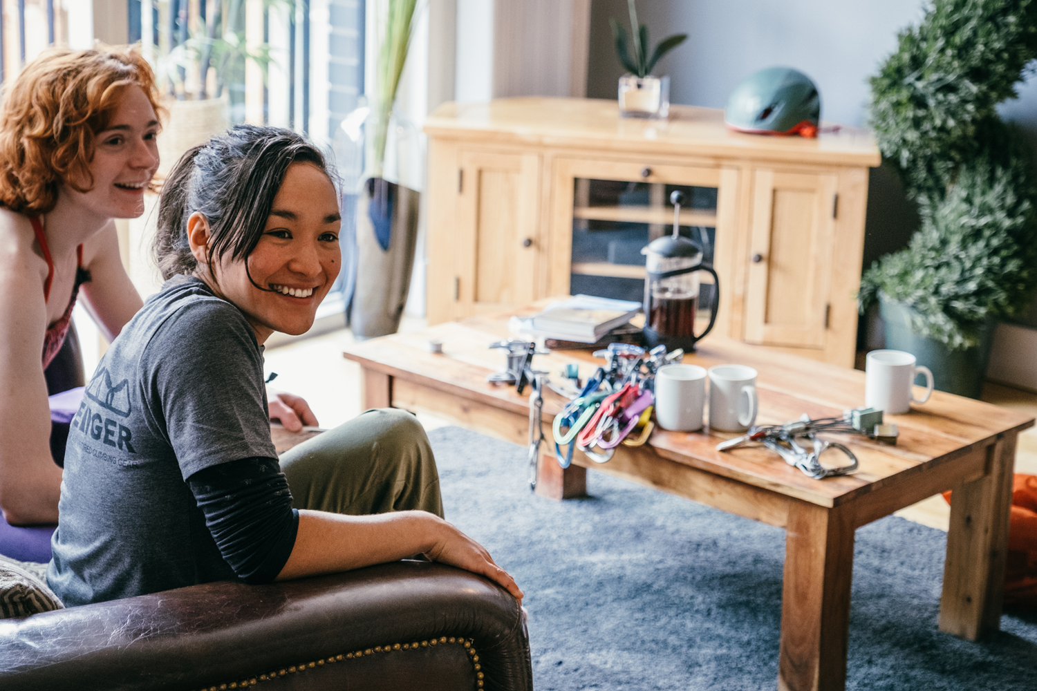 Two women are sat chatting together and drinking coffee in a living room.