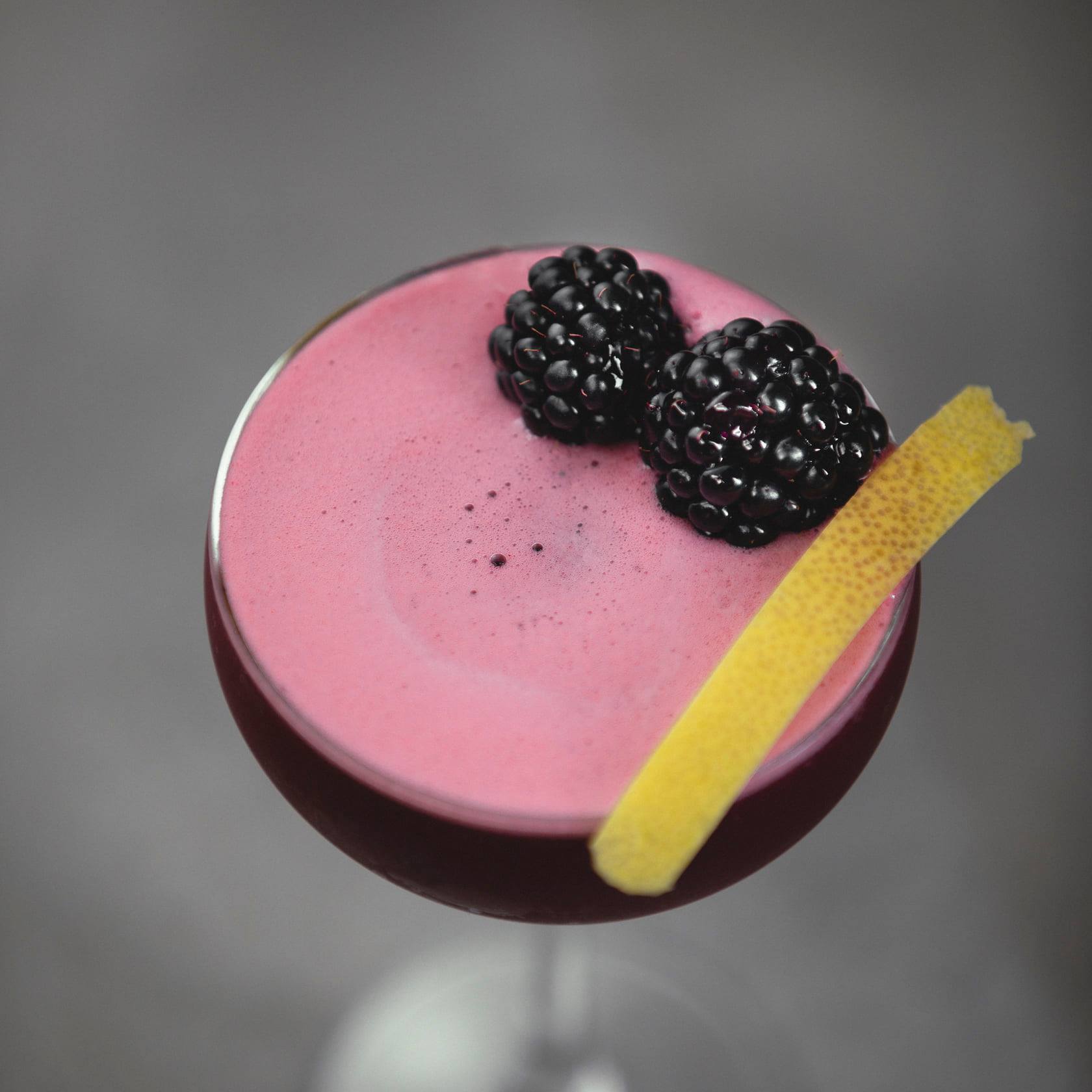  A red cocktail with two blackberries on top.