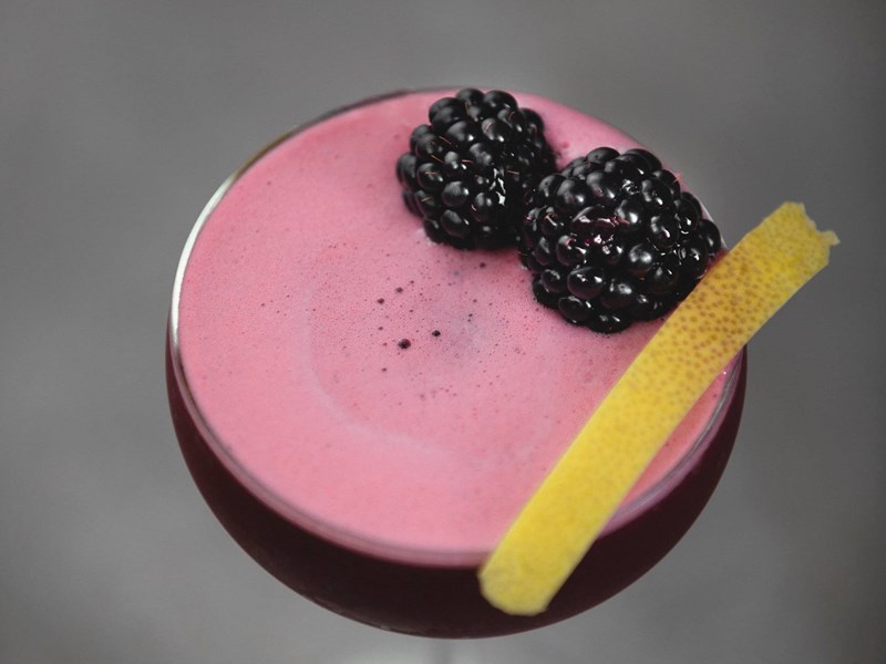 A red cocktail with two blackberries on top.