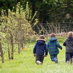 Three children running around in a field.