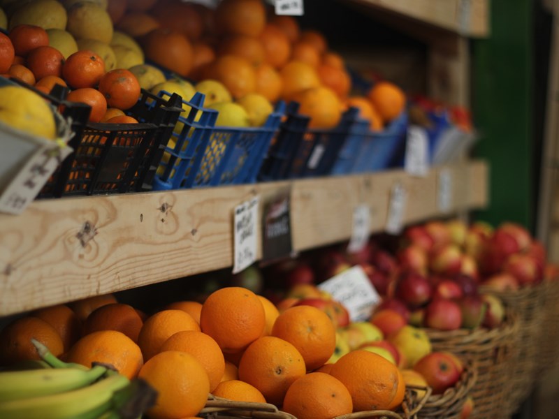 Wooden shelving with baskets full of oranges, apples, bananas and lemons.